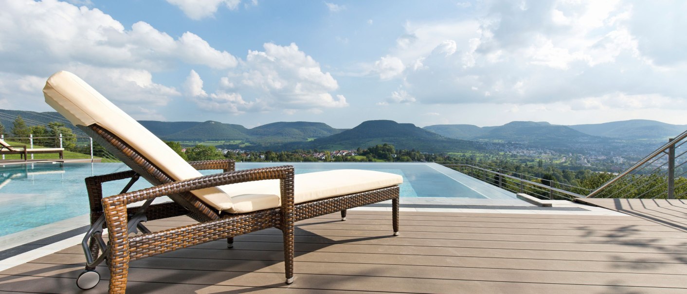 Ein Liegestuhl steht auf einer Terrasse neben einem Infinity-Pool. Im Hintergrund sind grüne Hügel und ein blauer Himmel mit Wolken zu sehen., © Achalm. Hotel GmbH & Co. KG Ein Liegestuhl steht auf einer Terrasse neben einem Infinity-Pool. Im Hintergrund sind grüne Hügel und ein blauer Himmel mit Wolken zu sehen., © Achalm. Hotel GmbH & Co. KG