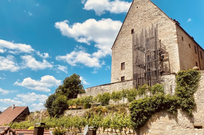 Ein historisches Gebäude mit Weinreben an einer Steinmauer unter einem klaren blauen Himmel mit weißen Wolken., © Stadt Besigheim Ein historisches Gebäude mit Weinreben an einer Steinmauer unter einem klaren blauen Himmel mit weißen Wolken., © Stadt Besigheim