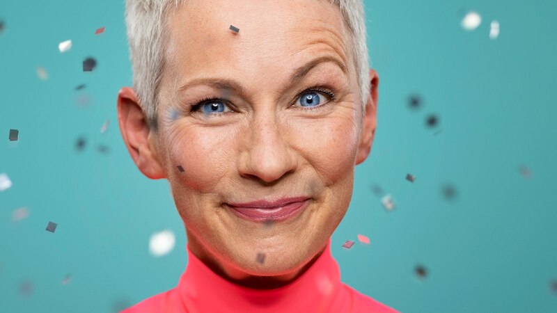 L&auml;chelnde Frau mit kurzem Haar vor t&uuml;rkisfarbenem Hintergrund, umgeben von Konfetti. Sie tr&auml;gt ein pinkes Oberteil. Foto von Jana Kay., &copy; Kultur- und Sportamt Stadt Bietigheim-Bissingen