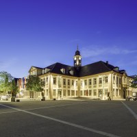 Beleuchtetes Rathaus bei Dämmerung, umgeben von Bäumen und modernen Gebäuden. Der leere Marktplatz im Vordergrund schafft eine ruhige Atmosphäre., © Stadtmarketing Göppingen
