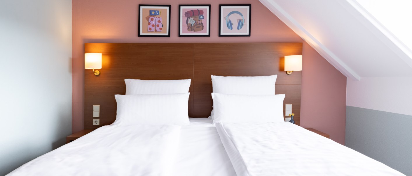 Ein stilvoll eingerichtetes Hotelzimmer mit einem gro&szlig;en Doppelbett, wei&szlig;en Bettlaken und Kissen. Drei Bilder schm&uuml;cken die Wand &uuml;ber dem Bett., &copy; Novum  Hospitality