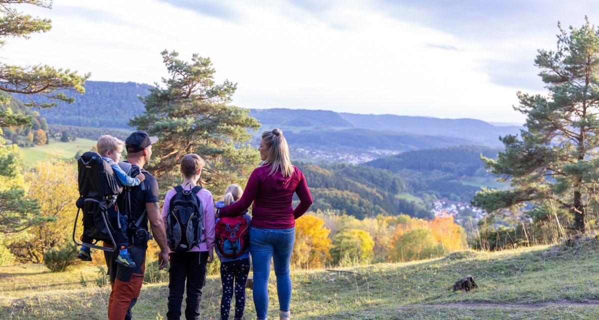 Eine Familie steht auf einem Hügel und blickt auf eine malerische Landschaft mit Wäldern und Hügeln. Die Sonne scheint durch die Bäume., © Foto Thomas Zehnder Eine Familie steht auf einem Hügel und blickt auf eine malerische Landschaft mit Wäldern und Hügeln. Die Sonne scheint durch die Bäume., © Foto Thomas Zehnder
