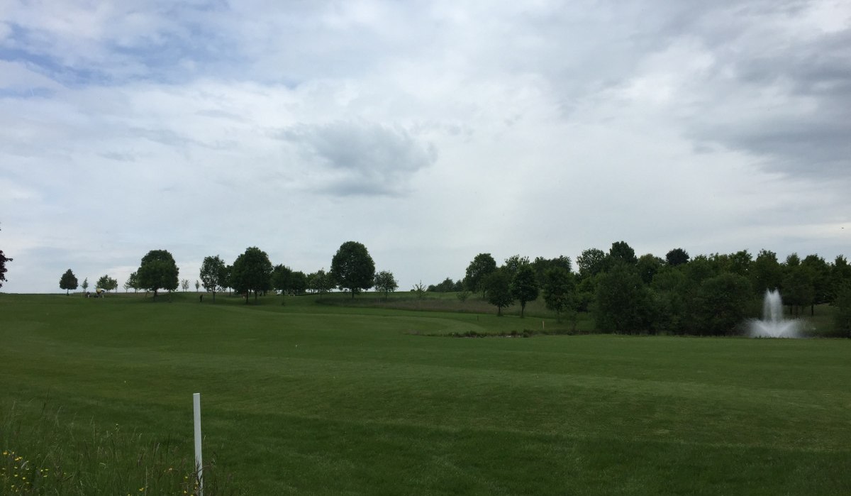 Weitläufiger Golfplatz mit grüner Wiese, Bäumen und einem Springbrunnen. Der Himmel ist bewölkt., © www.pro-cycl.de