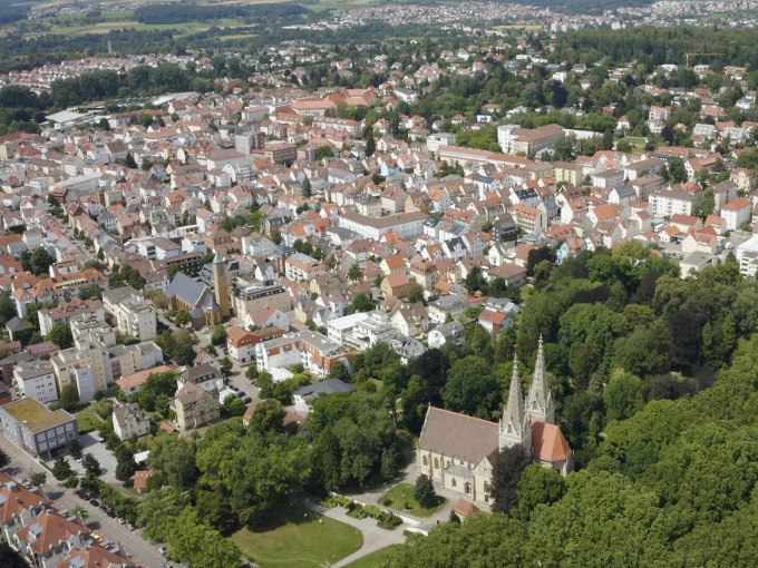 Luftaufnahme einer Stadt mit dicht bebauten Häusern und einer markanten Kirche, umgeben von grünen Bäumen und Parks., © Stadt Göppingen Luftaufnahme einer Stadt mit dicht bebauten Häusern und einer markanten Kirche, umgeben von grünen Bäumen und Parks., © Stadt Göppingen