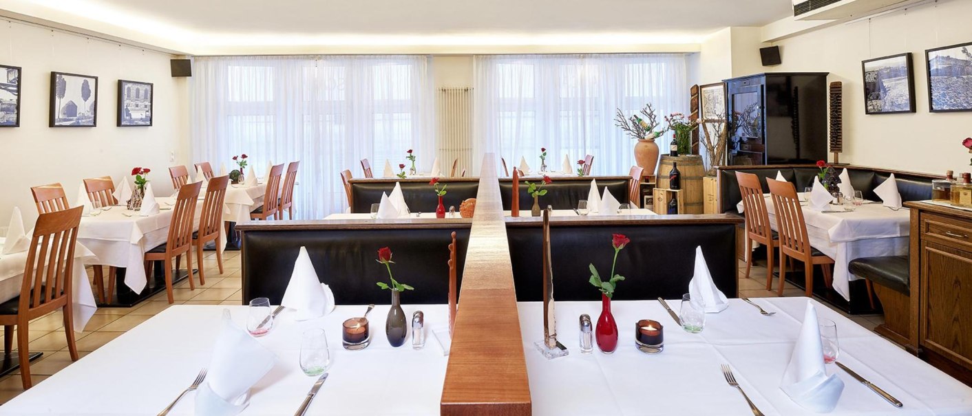 Elegantes Restaurant mit weißen Tischdecken, Holzstühlen und dekorativen Rosen auf den Tischen. Helle, einladende Atmosphäre., © Frank Pham