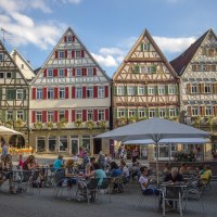 Fachwerkhäuser am Marktplatz in Herrenberg, Menschen sitzen an Tischen im Freien unter Sonnenschirmen, blauer Himmel im Hintergrund., © Natur.Nah. Schönbuch & Heckengäu
