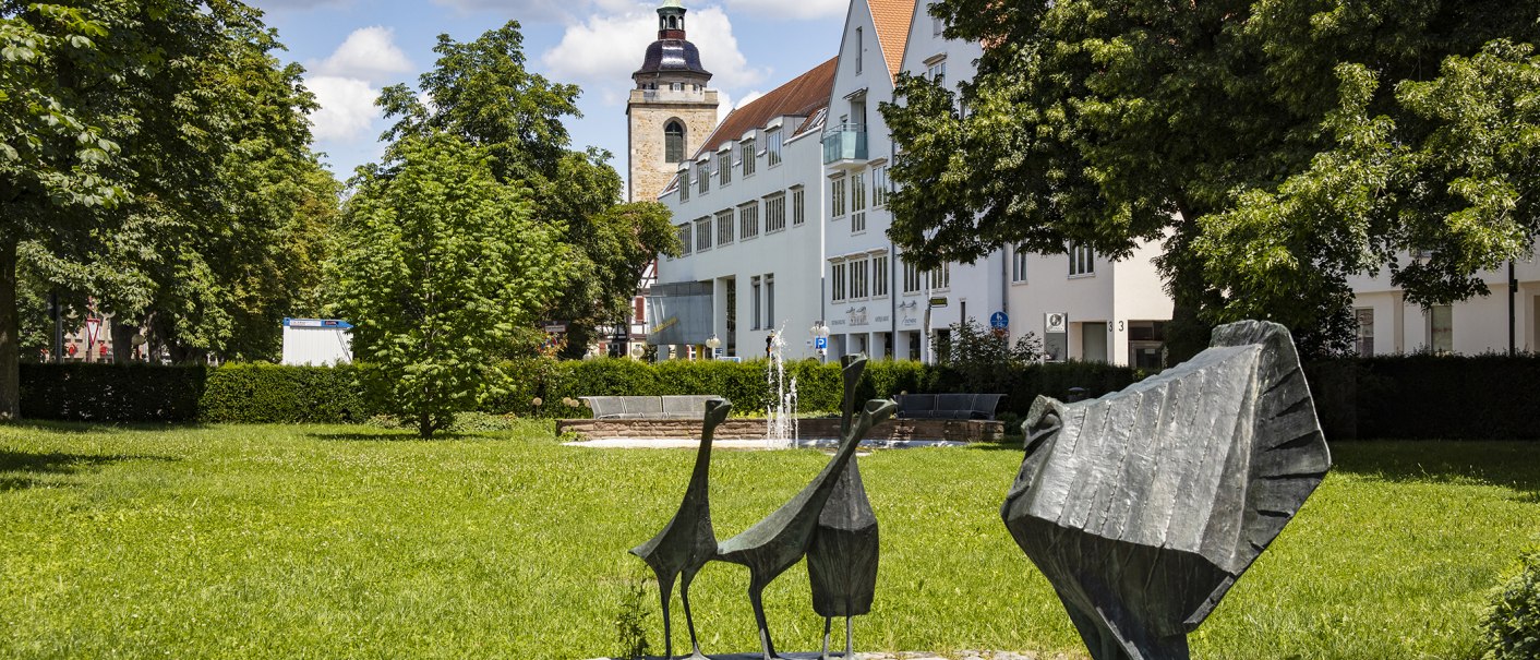 Grüne Parklandschaft mit modernen Skulpturen im Vordergrund, einem Brunnen und einem Kirchturm im Hintergrund in Kirchheim unter Teck., © Torsten Wenzler