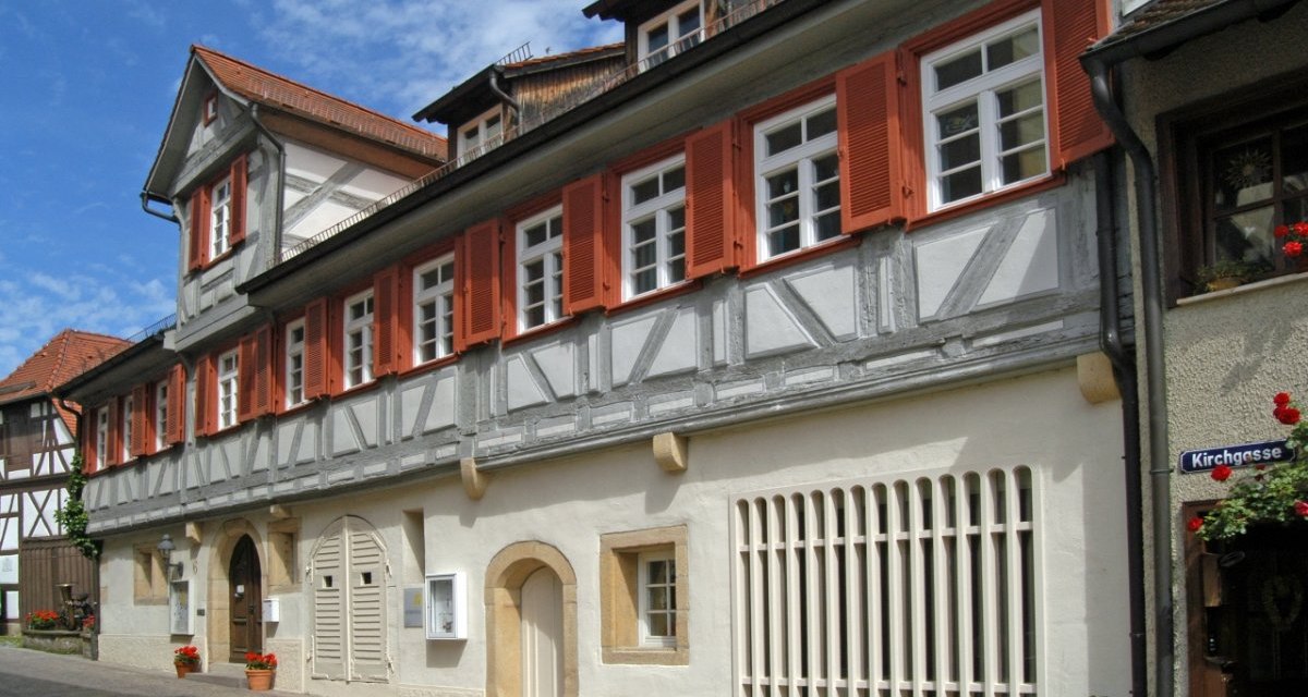 Fachwerkhaus mit roten Fensterl&auml;den in einer engen Gasse. Das Geb&auml;ude hat ein traditionelles Design mit wei&szlig;en und grauen Elementen., &copy; Natur.Nah. Sch&ouml;nbuch & Heckeng&auml;u