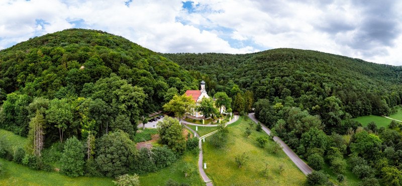 Luftaufnahme der Wallfahrtskirche Ave Maria Deggingen, eingebettet in eine grüne Waldlandschaft mit Hügeln im Hintergrund., © Landkreis Göppingen Luftaufnahme der Wallfahrtskirche Ave Maria Deggingen, eingebettet in eine grüne Waldlandschaft mit Hügeln im Hintergrund., © Landkreis Göppingen