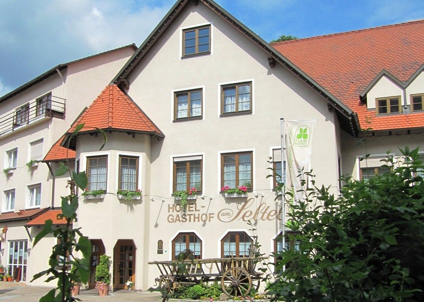 Hotel-Gasthof mit traditionellem Fachwerk, Blumenkästen und einem alten Holzwagen davor. Der Himmel ist blau mit einigen Wolken., © R.Storr