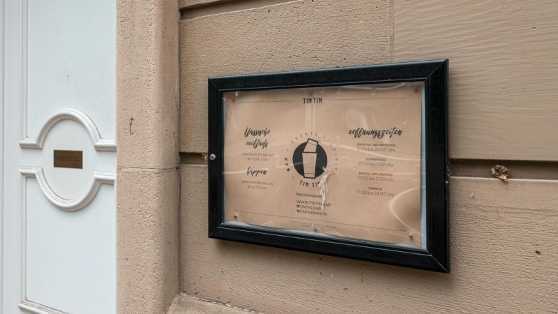Schild der TinTin Bar mit Öffnungszeiten und Preisen an einer Wand neben einer weißen Tür., © SMG, Sarah Schmid Schild der TinTin Bar mit Öffnungszeiten und Preisen an einer Wand neben einer weißen Tür., © SMG, Sarah Schmid