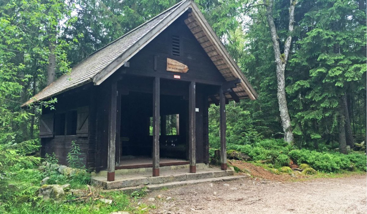 Eine kleine Holzhütte im Wald, umgeben von hohen Bäumen. Über dem Eingang hängt ein Schild. Der Boden ist mit Kies bedeckt., © www.pro-cycl.de Eine kleine Holzhütte im Wald, umgeben von hohen Bäumen. Über dem Eingang hängt ein Schild. Der Boden ist mit Kies bedeckt., © www.pro-cycl.de