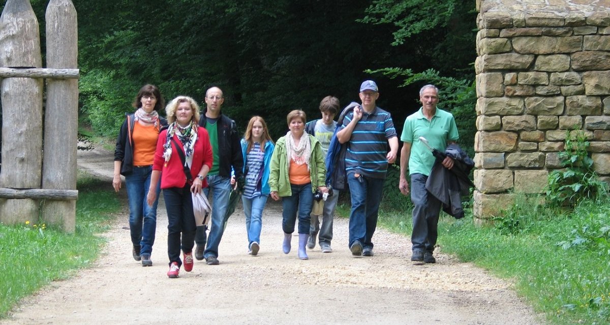 Eine Gruppe von acht Personen wandert auf einem Waldweg neben einer Steinmauer und Holztor. Sie sind lässig gekleidet und scheinen entspannt., © Stadtverwaltung Schwäbisch Gmünd Eine Gruppe von acht Personen wandert auf einem Waldweg neben einer Steinmauer und Holztor. Sie sind lässig gekleidet und scheinen entspannt., © Stadtverwaltung Schwäbisch Gmünd