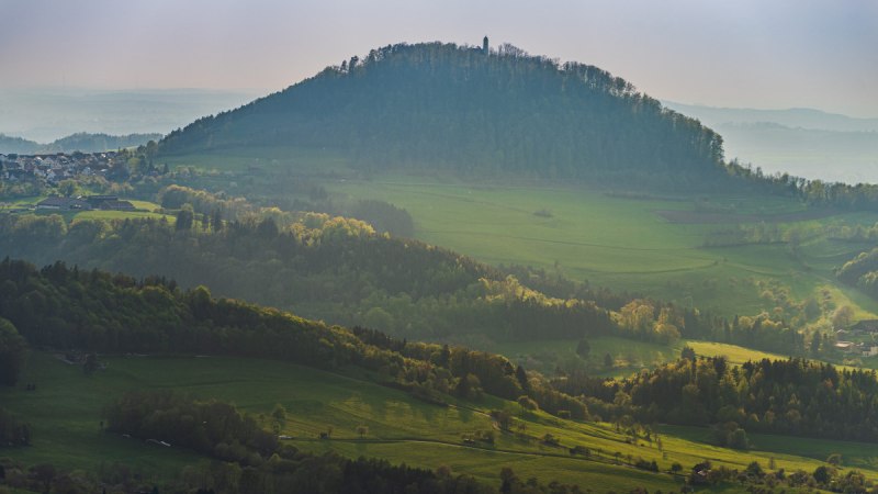Der Rechberg erhebt sich majest&auml;tisch &uuml;ber die umliegenden gr&uuml;nen Wiesen und W&auml;lder, w&auml;hrend die Sonne sanft die Landschaft beleuchtet.