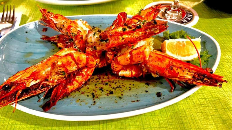 Gegrillte Garnelen auf blauem Teller mit Kräutern und Zitronenscheibe, auf grünem Tisch serviert., © Restaurant Neckarau, P. Kotaidis Gegrillte Garnelen auf blauem Teller mit Kräutern und Zitronenscheibe, auf grünem Tisch serviert., © Restaurant Neckarau, P. Kotaidis