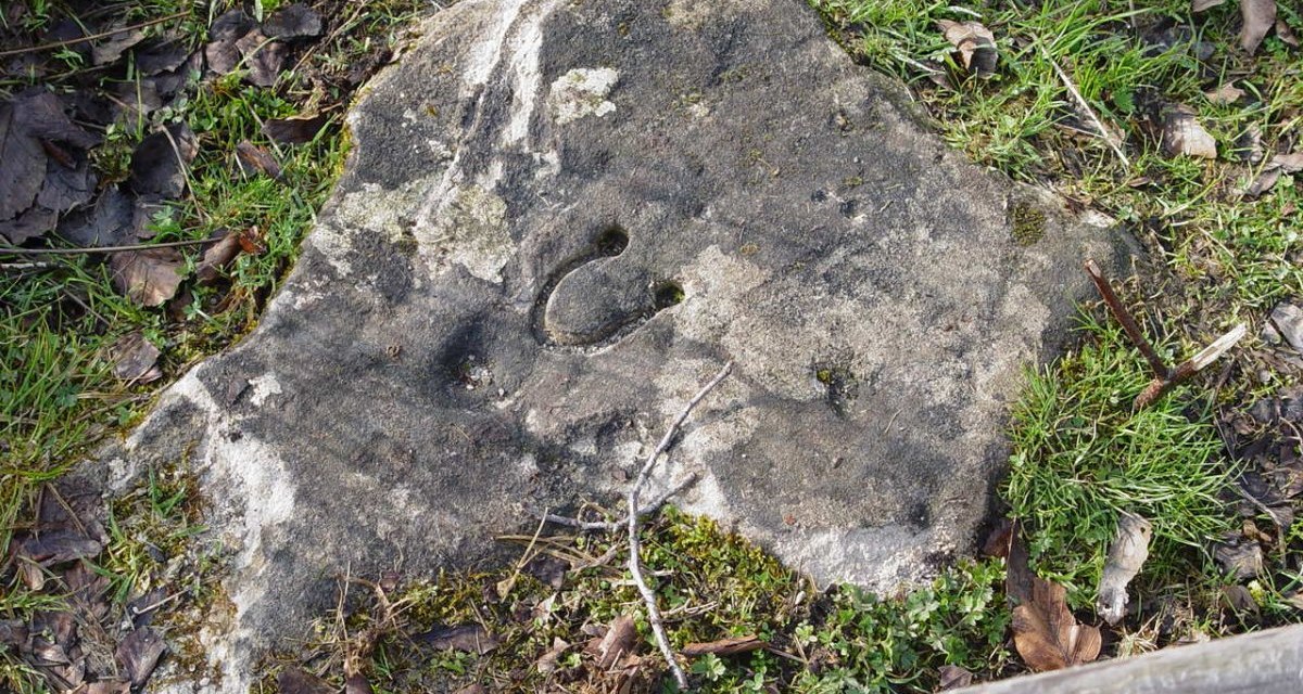 Ein gro&szlig;er Stein mit einer eingravierten Hufeisenform liegt auf grasbewachsenem Boden, umgeben von Laub und Holz., &copy; Naturpark Sch&ouml;nbuch