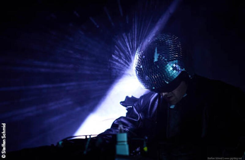 Person mit Disco-Kugel-Helm in dunkler Umgebung, umgeben von Lichteffekten. Die Szene wirkt futuristisch und geheimnisvoll., © Stadt Kornwestheim Kulturmanagement