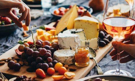 Eine ansprechend angerichtete K&auml;seplatte mit Trauben, N&uuml;ssen und einem Glas Ros&eacute;wein auf einem Tisch., &copy; Wein & K&auml;se. Foto: Teamwerk