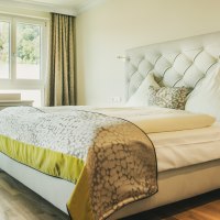 Helles Hotelzimmer mit gro&szlig;em Bett, Schreibtisch und Blick auf Wasser und Berge durch die Fenster., &copy; LOCHER Fotodesign & Manufaktur