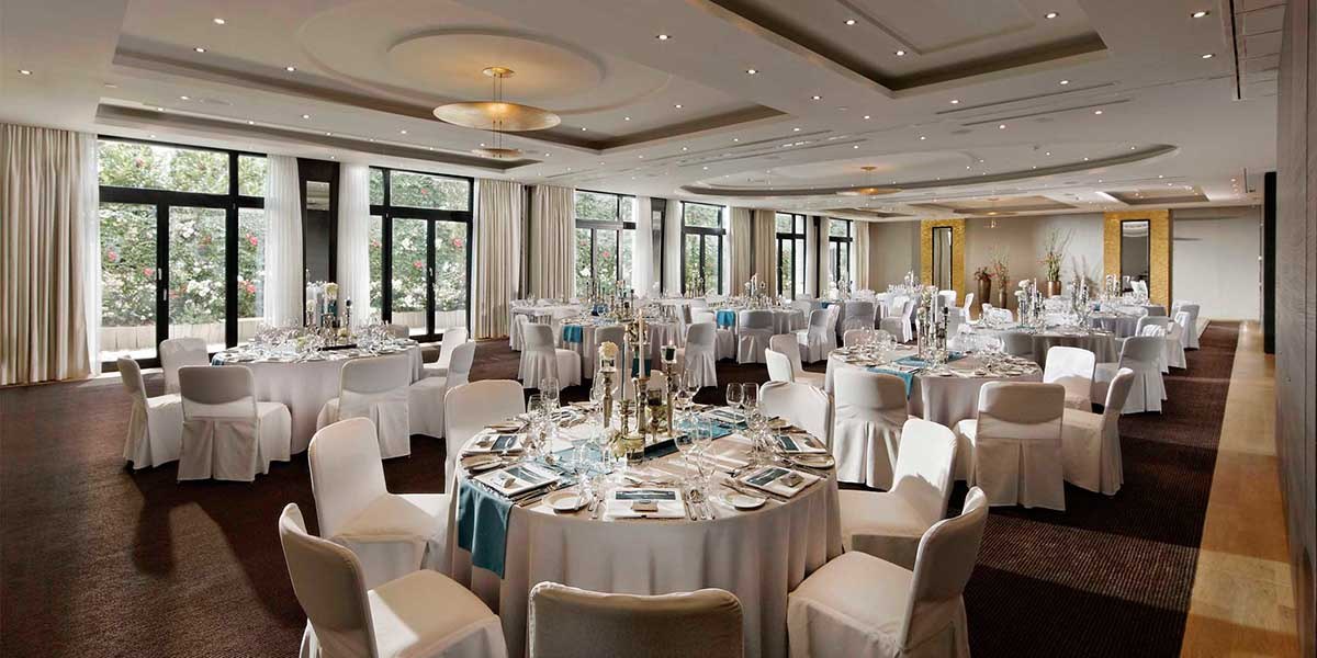 Eleganter Ballsaal mit runden, weiß gedeckten Tischen und Stühlen, dekoriert für eine Veranstaltung., © Parkhotel Stuttgart Messe-Airport