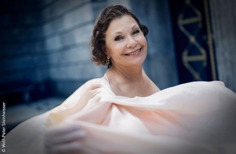 Eine Frau in einem fließenden, eleganten Kleid lächelt freundlich in die Kamera. Der Hintergrund ist unscharf und zeigt eine Steinmauer., © Stadt Kornwestheim Kulturmanagement