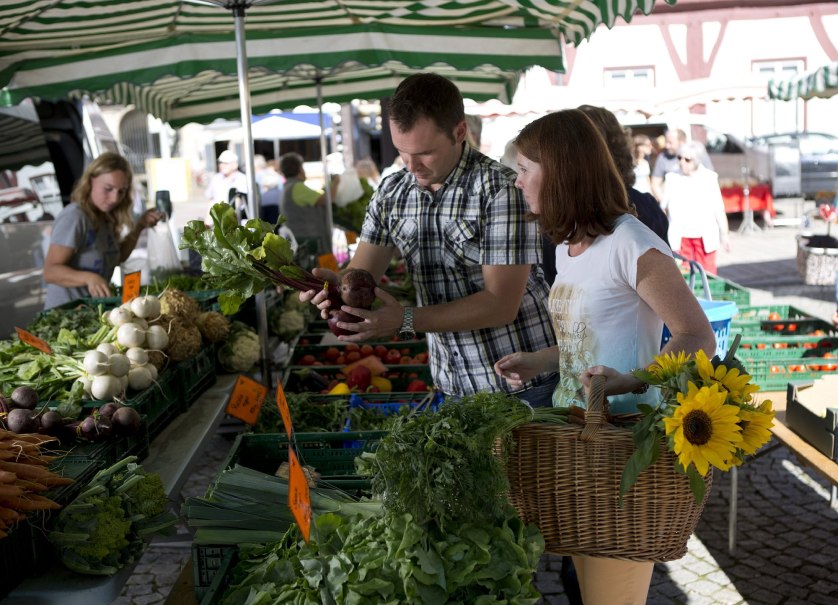 Menschen kaufen frisches Gemüse auf einem Wochenmarkt. Ein Mann hält Rote Bete, eine Frau trägt einen Korb mit Sonnenblumen. Im Hintergrund sind Marktstände., © Bad Urach Tourismus Menschen kaufen frisches Gemüse auf einem Wochenmarkt. Ein Mann hält Rote Bete, eine Frau trägt einen Korb mit Sonnenblumen. Im Hintergrund sind Marktstände., © Bad Urach Tourismus