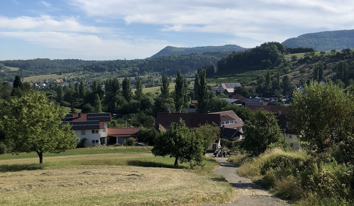 Blick auf ein Dorf in einer hügeligen Landschaft mit grünen Wiesen und Bäumen unter einem blauen Himmel mit weißen Wolken., © Touristik und Marketing GmbH Blick auf ein Dorf in einer hügeligen Landschaft mit grünen Wiesen und Bäumen unter einem blauen Himmel mit weißen Wolken., © Touristik und Marketing GmbH