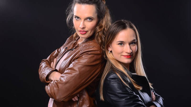 Zwei Frauen in Lederjacken stehen Rücken an Rücken und lächeln in die Kamera. Der Hintergrund ist schwarz, was die Personen hervorhebt., © Kammerkonzerte Schwäbisch Hall e.V.