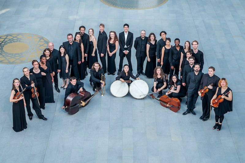 Ein Orchester in schwarzer Kleidung steht in einem Kreis auf einem grauen Boden mit goldenen Mustern., &copy; Kulturstiftung Hohenlohe