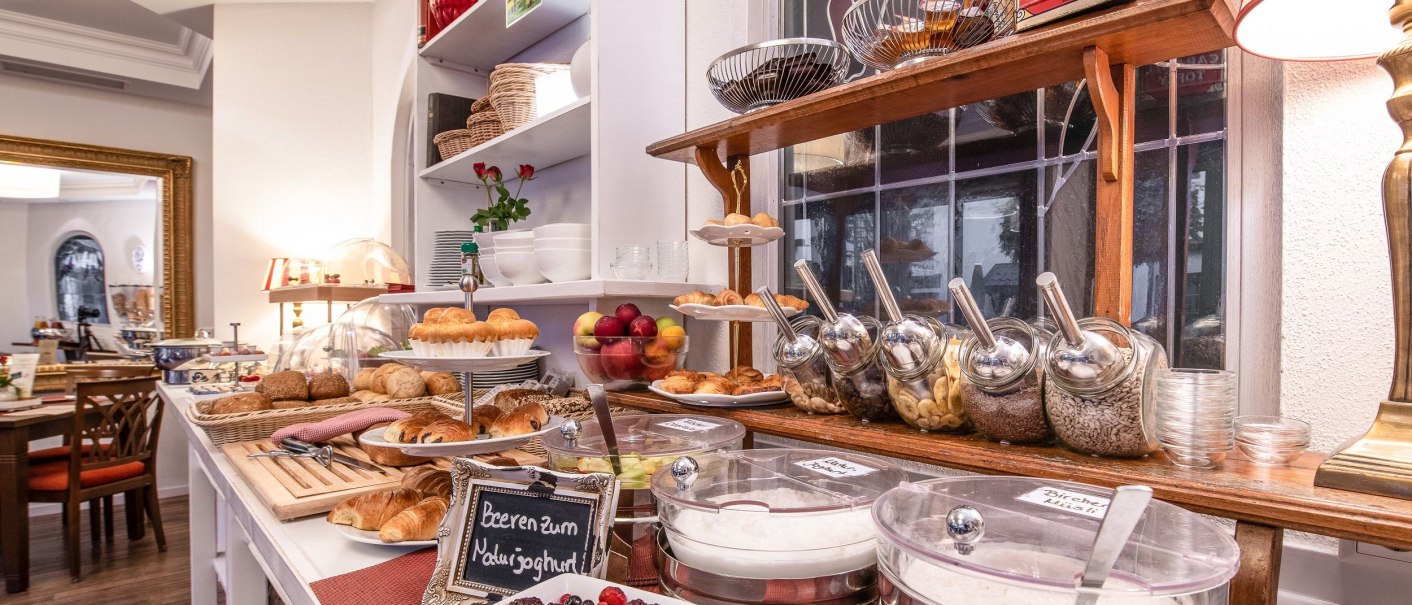 Ein reichhaltiges Frühstücksbuffet mit Brötchen, Croissants, Joghurt, Beeren und Müsli in einem stilvollen Raum., © Hotel Weinstadt