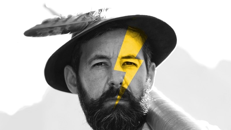 Ein Mann mit traditionellem Hut und Bart trägt ein Alphorn. Ein gelber Blitz ziert sein Gesicht, was einen modernen Touch verleiht., © Kulturhaus Schwanen Ein Mann mit traditionellem Hut und Bart trägt ein Alphorn. Ein gelber Blitz ziert sein Gesicht, was einen modernen Touch verleiht., © Kulturhaus Schwanen