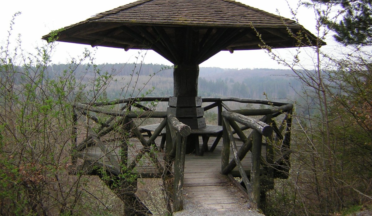 Ein hölzerner Aussichtspunkt mit Dach, umgeben von Bäumen und Sträuchern, bietet einen Blick auf bewaldete Hügel im Hintergrund., © Naturpark Schönbuch Ein hölzerner Aussichtspunkt mit Dach, umgeben von Bäumen und Sträuchern, bietet einen Blick auf bewaldete Hügel im Hintergrund., © Naturpark Schönbuch