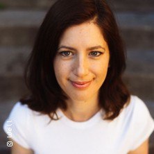 Eine Frau mit braunen Haaren und wei&szlig;em T-Shirt l&auml;chelt in die Kamera. Der Hintergrund ist unscharf., &copy; links im Bild