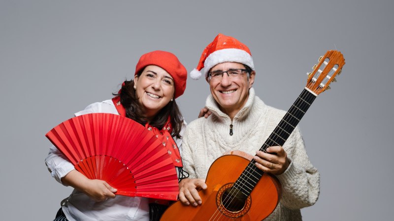 Ein Mann und eine Frau tragen Weihnachtsm&uuml;tzen. Die Frau h&auml;lt einen roten F&auml;cher, der Mann eine Gitarre. Beide l&auml;cheln in die Kamera., &copy; Duo Alegria