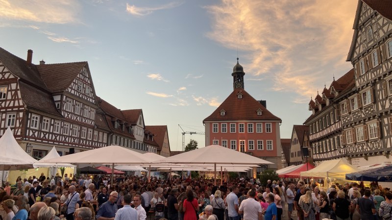 Weinfest in Schorndorf: Menschen genießen den Abend auf einem Platz mit Fachwerkhäusern und Zelten, während der Himmel in warmen Farben leuchtet., © Stadt Schorndorf Weinfest in Schorndorf: Menschen genießen den Abend auf einem Platz mit Fachwerkhäusern und Zelten, während der Himmel in warmen Farben leuchtet., © Stadt Schorndorf