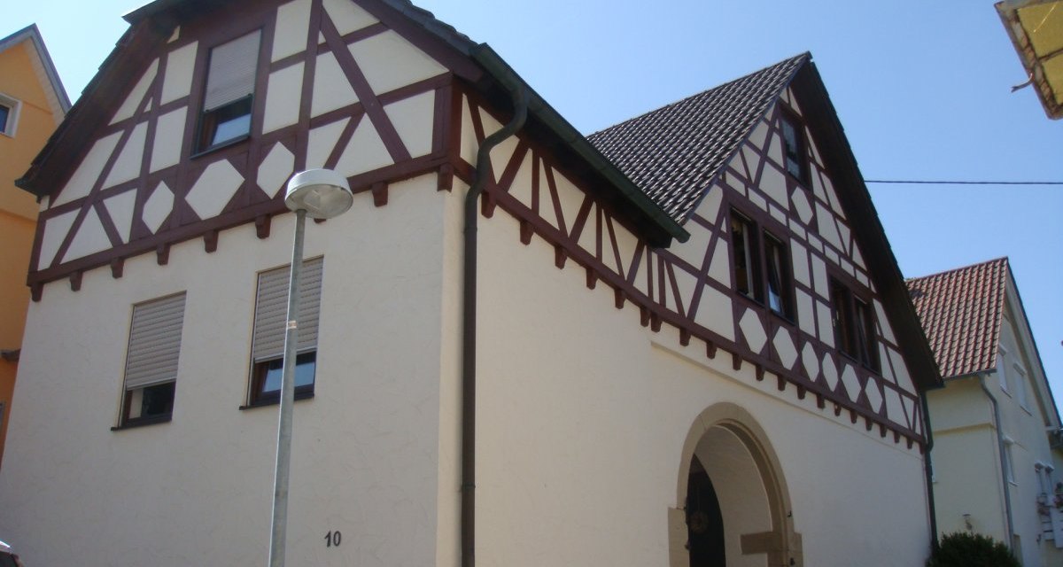 Fachwerkhaus mit weißer Fassade und braunen Balken, Satteldach und Rundbogeneingang. Eine Straßenlaterne steht davor., © Land der 1000 Hügel - Kraichgau-Stromberg Fachwerkhaus mit weißer Fassade und braunen Balken, Satteldach und Rundbogeneingang. Eine Straßenlaterne steht davor., © Land der 1000 Hügel - Kraichgau-Stromberg