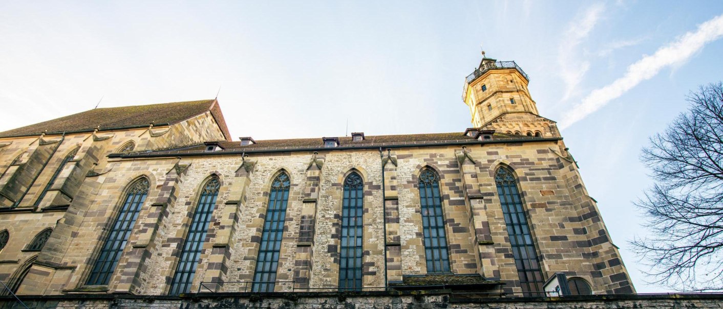 Seitenansicht der Michaelskirche in Schwäbisch Hall mit gotischen Fenstern und einem Turm vor blauem Himmel., © Stuttgart-Marketing GmbH, Sarah Schmid Seitenansicht der Michaelskirche in Schwäbisch Hall mit gotischen Fenstern und einem Turm vor blauem Himmel., © Stuttgart-Marketing GmbH, Sarah Schmid