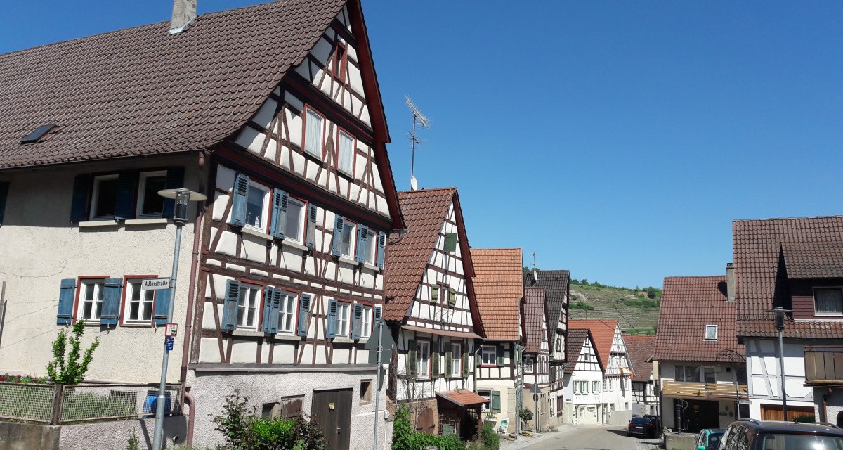 Fachwerkhäuser in Rosswag unter klarem, blauem Himmel. Die Straße ist gesäumt von geparkten Autos und traditionellen Gebäuden., © Land der 1000 Hügel - Kraichgau-Stromberg
