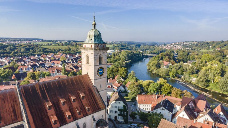 Drohnenansicht der Stadtkirche am Neckar, umgeben von roten D&auml;chern und gr&uuml;ner Landschaft. Der Fluss schl&auml;ngelt sich durch die Stadt., &copy; Stadplanungsamt Stadt N&uuml;rtingen; artismedia GmbH/ Olaf K&uuml;hl