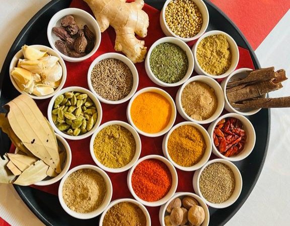 Ein rundes Tablett mit verschiedenen Gewürzen in kleinen Schalen, darunter Ingwer, Knoblauch, Zimtstangen und bunte Gewürzpulver., © Sangam Ein rundes Tablett mit verschiedenen Gewürzen in kleinen Schalen, darunter Ingwer, Knoblauch, Zimtstangen und bunte Gewürzpulver., © Sangam