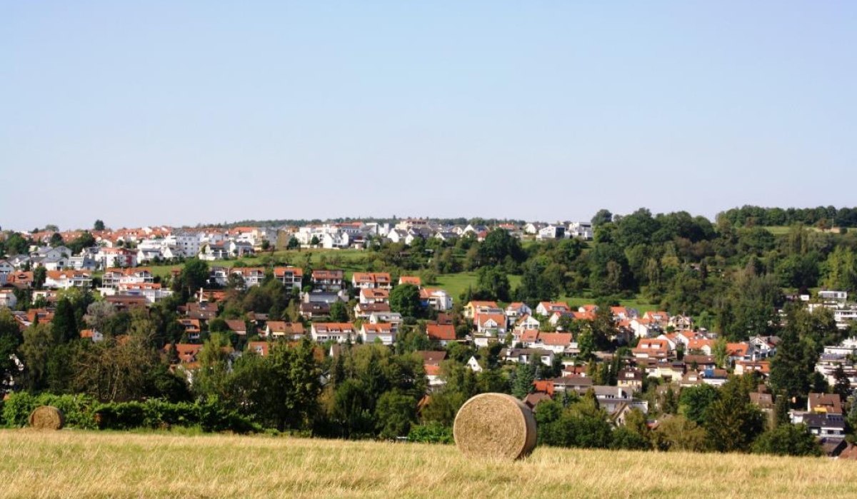 Ein Heuballen auf einem Feld mit Blick auf ein Wohngebiet mit roten Dächern und grünen Bäumen im Hintergrund., © Natur.Nah. Schönbuch & Heckengäu Ein Heuballen auf einem Feld mit Blick auf ein Wohngebiet mit roten Dächern und grünen Bäumen im Hintergrund., © Natur.Nah. Schönbuch & Heckengäu