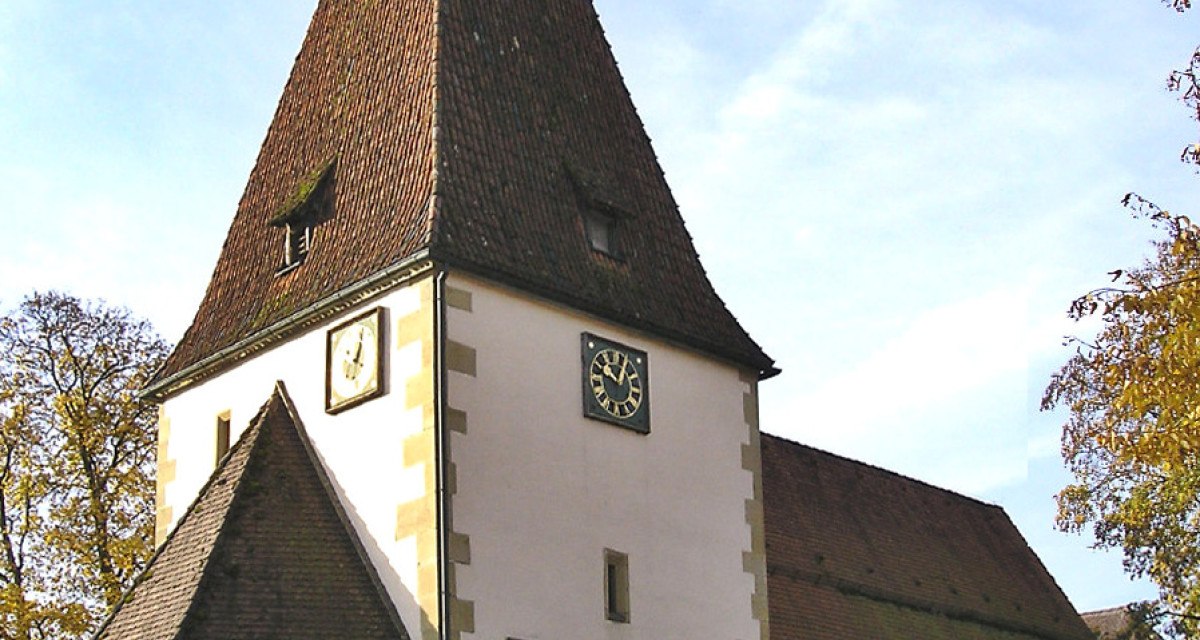 Die Afra Kirche in Täferrot mit spitzem Turm, Uhr und weißen Wänden, umgeben von Bäumen und blauem Himmel., © Gemeindeverwaltung Täferrot Die Afra Kirche in Täferrot mit spitzem Turm, Uhr und weißen Wänden, umgeben von Bäumen und blauem Himmel., © Gemeindeverwaltung Täferrot