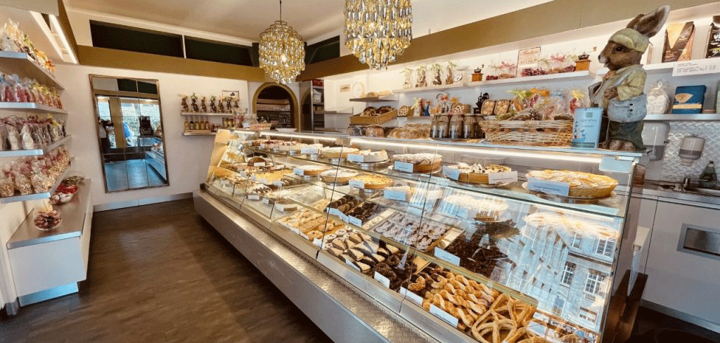 Ein gemütliches Café mit einer Vitrine voller Gebäck und Schokolade. Dekorative Figuren und ein Kronleuchter ergänzen das Ambiente., © FreCla Gastronomiebetriebe GmbH