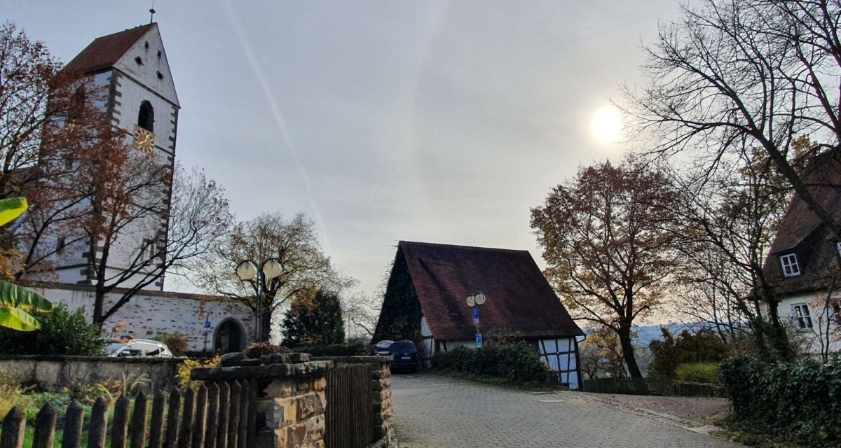Herbstliche Szene in Kirchberg mit einer Kirche, einem Fachwerkhaus und kahlen Bäumen unter einem bewölkten Himmel., © Kulturamt Plochingen Herbstliche Szene in Kirchberg mit einer Kirche, einem Fachwerkhaus und kahlen Bäumen unter einem bewölkten Himmel., © Kulturamt Plochingen