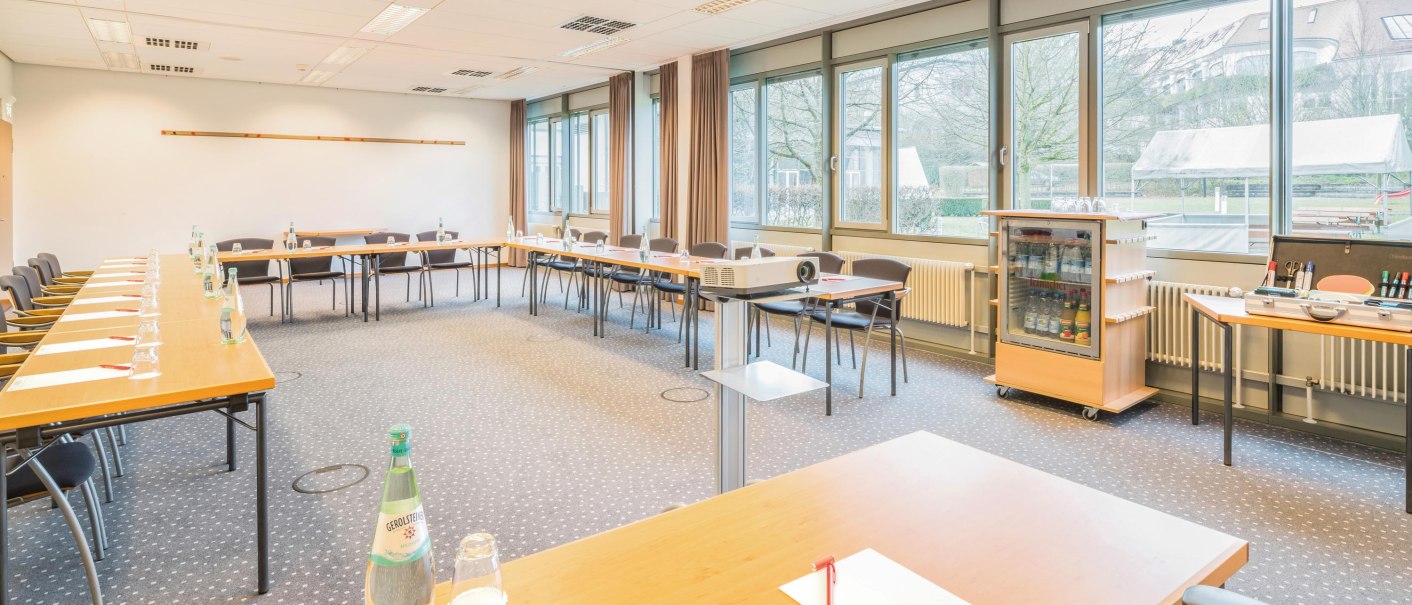 Heller Tagungsraum mit U-förmiger Tischanordnung, Stühlen, Projektor und großen Fenstern. Auf den Tischen stehen Wasserflaschen und Schreibmaterialien., © Seminaris Hotel Bad Boll Heller Tagungsraum mit U-förmiger Tischanordnung, Stühlen, Projektor und großen Fenstern. Auf den Tischen stehen Wasserflaschen und Schreibmaterialien., © Seminaris Hotel Bad Boll