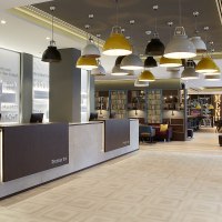 Moderne Hotel-Lobby mit Rezeption, hängenden Lampen und gemütlichem Sitzbereich. An der Wand steht "Premier Inn". Im Hintergrund ist eine Lounge sichtbar., © Premier Inn Moderne Hotel-Lobby mit Rezeption, hängenden Lampen und gemütlichem Sitzbereich. An der Wand steht "Premier Inn". Im Hintergrund ist eine Lounge sichtbar., © Premier Inn