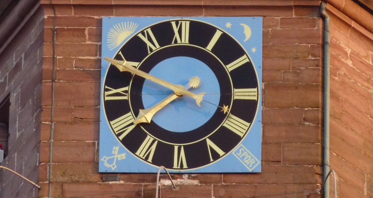 Gro&szlig;e Uhr mit r&ouml;mischen Ziffern auf blauem Hintergrund an einem Backsteingeb&auml;ude. Verzierungen mit Sonne, Mond und Sternen., &copy; Natur.Nah. Sch&ouml;nbuch & Heckeng&auml;u