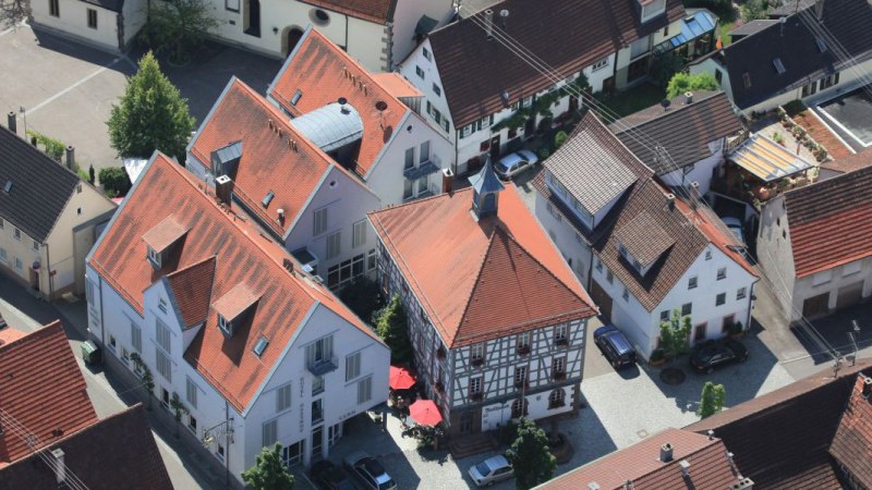 Luftaufnahme eines Dorfes mit Fachwerkhäusern und roten Dächern. Im Zentrum ein Gebäude mit rotem Dach und Sonnenschirmen., © Hotel Gasthof Lamm