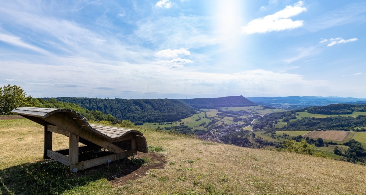 Holzliege am Aussichtspunkt mit Blick auf gr&uuml;ne H&uuml;gel und T&auml;ler unter blauem Himmel., &copy; Foto Thomas Zehnder