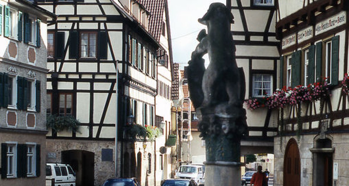 Ein malerischer Marktplatz mit Fachwerkhäusern und einem Brunnen, umgeben von roten Blumen. Autos parken entlang der Straße., © Stadt Wiesensteig Ein malerischer Marktplatz mit Fachwerkhäusern und einem Brunnen, umgeben von roten Blumen. Autos parken entlang der Straße., © Stadt Wiesensteig